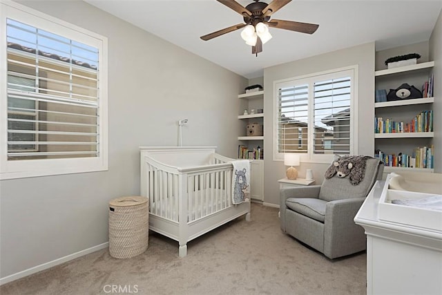 bedroom featuring a crib, a ceiling fan, baseboards, and light carpet