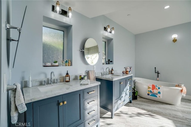 full bath featuring a sink, a freestanding bath, two vanities, and recessed lighting