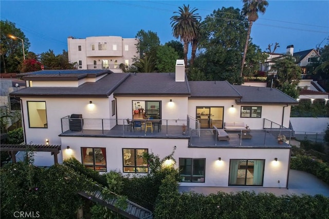 back of house with stucco siding, a pergola, central AC, a balcony, and a chimney