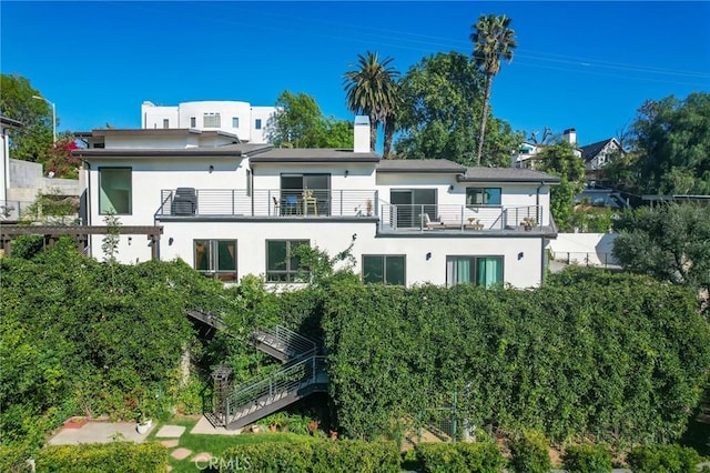 back of property featuring stairway, stucco siding, a chimney, and a balcony