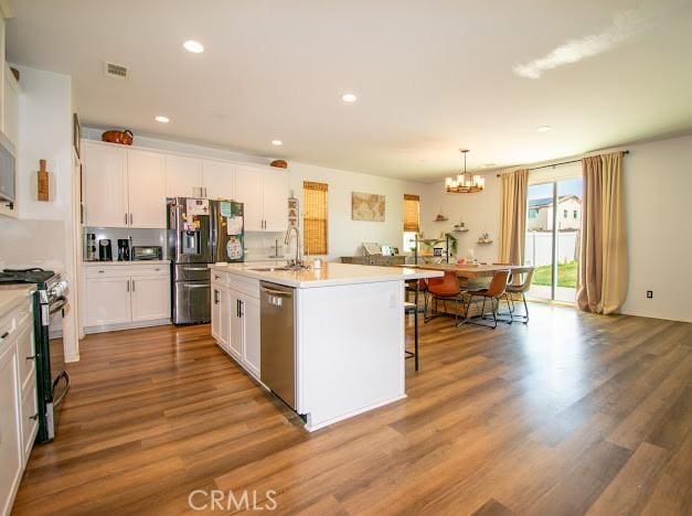 kitchen with a sink, stainless steel appliances, an inviting chandelier, and wood finished floors