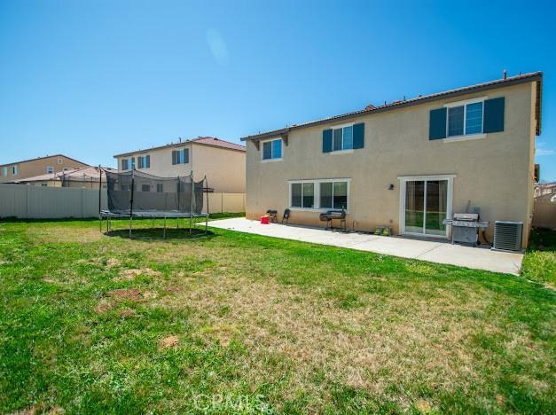 back of house featuring a trampoline, a lawn, and stucco siding