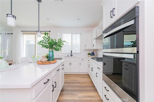 kitchen with light wood-style flooring, a sink, stainless steel appliances, light countertops, and pendant lighting