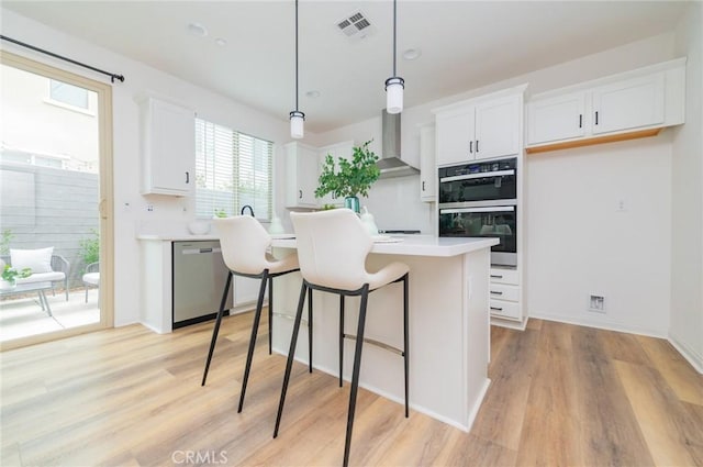 kitchen featuring visible vents, wall chimney range hood, double wall oven, white cabinetry, and stainless steel dishwasher