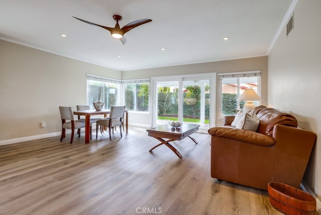 living room featuring light wood-style floors, visible vents, a wealth of natural light, and ornamental molding