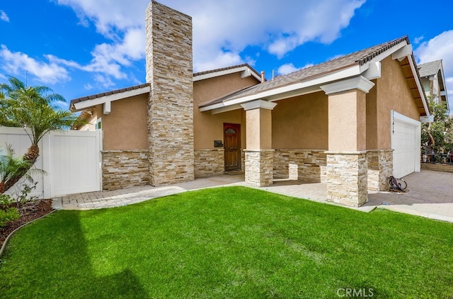 rear view of property featuring stone siding, stucco siding, an attached garage, and fence