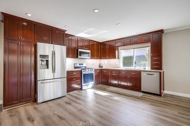 kitchen with light stone counters, tasteful backsplash, light wood-type flooring, and appliances with stainless steel finishes