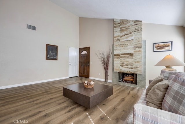 living room featuring a tiled fireplace, wood finished floors, visible vents, and baseboards