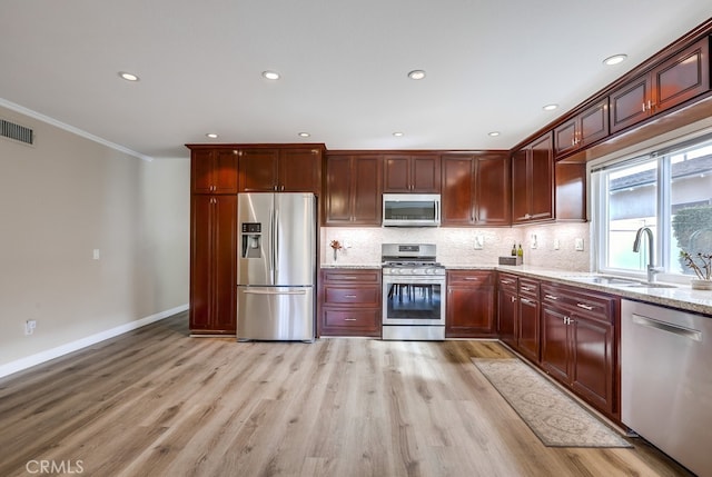 kitchen featuring a sink, backsplash, stainless steel appliances, light wood finished floors, and light stone countertops