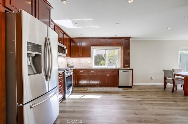 kitchen with light wood finished floors, plenty of natural light, backsplash, and appliances with stainless steel finishes