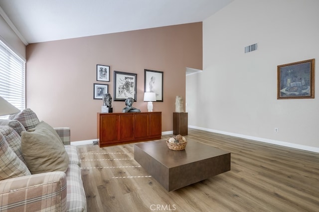 living area featuring visible vents, high vaulted ceiling, light wood-style floors, and baseboards