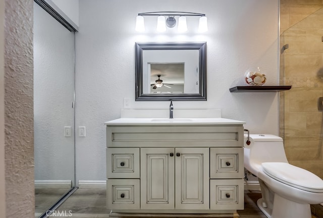 bathroom featuring toilet, wood finished floors, tiled shower, ceiling fan, and vanity