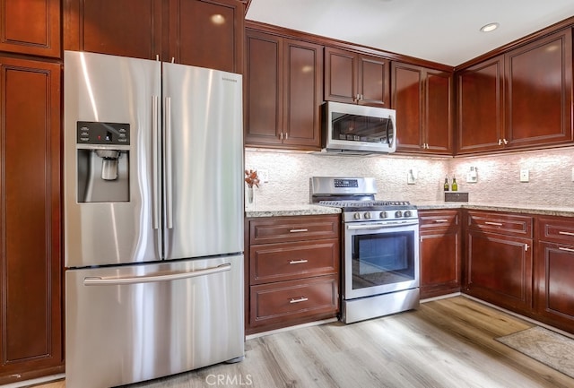 kitchen with light stone counters, stainless steel appliances, light wood-style floors, and decorative backsplash