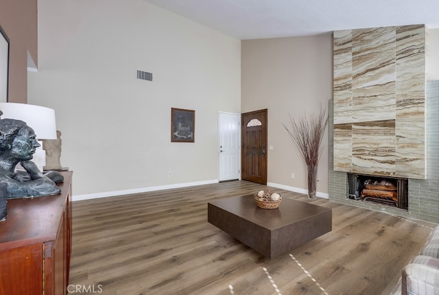 living room featuring a tiled fireplace, visible vents, baseboards, and wood finished floors