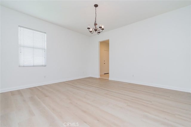 spare room featuring a notable chandelier, baseboards, and light wood finished floors