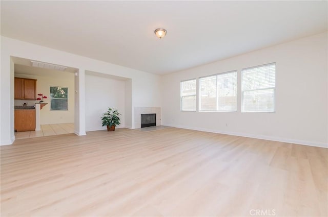 unfurnished living room with visible vents, a tile fireplace, light wood-type flooring, and baseboards