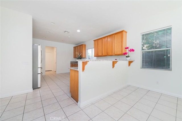 kitchen with light stone countertops, a breakfast bar area, light tile patterned floors, a peninsula, and freestanding refrigerator