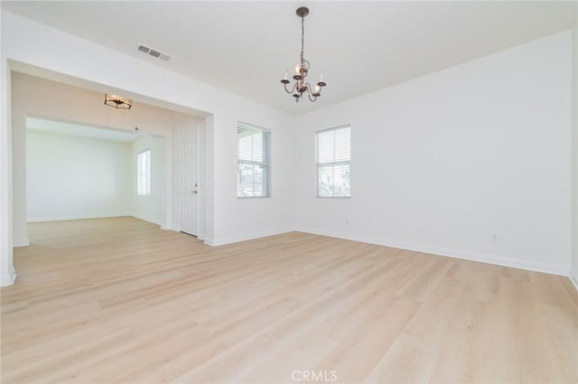 empty room with baseboards, visible vents, light wood finished floors, and a chandelier