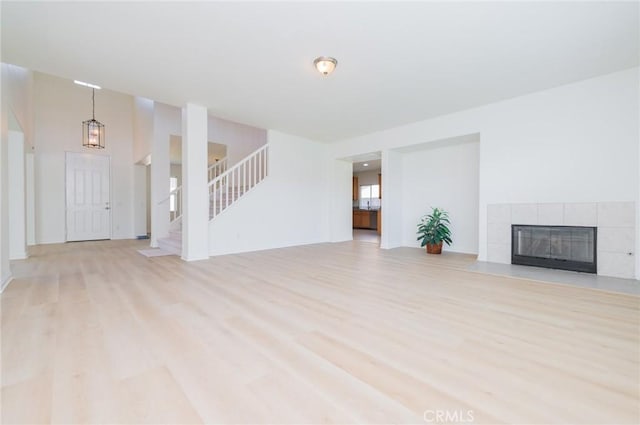 unfurnished living room with light wood-type flooring, stairs, and a tile fireplace