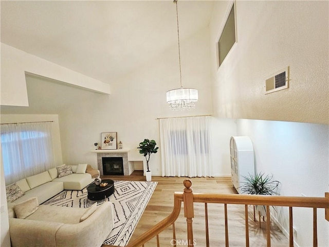 living room with visible vents, a fireplace with flush hearth, a notable chandelier, wood finished floors, and a towering ceiling