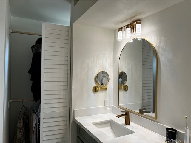 bathroom with a walk in closet, vanity, and a textured wall