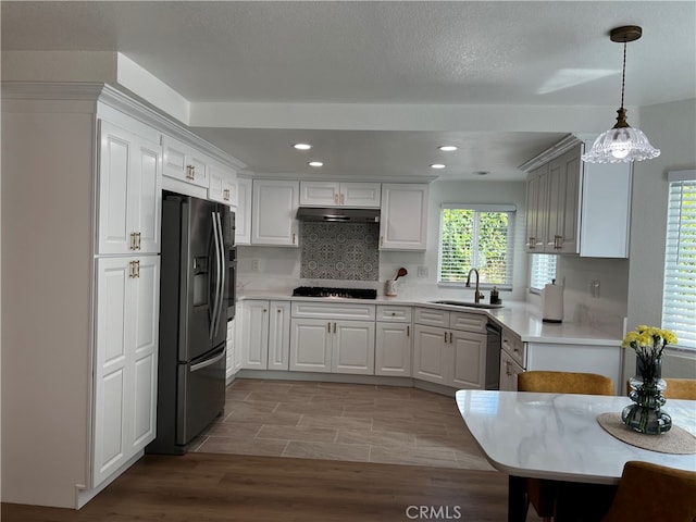 kitchen featuring wood finish floors, black appliances, a sink, under cabinet range hood, and light countertops