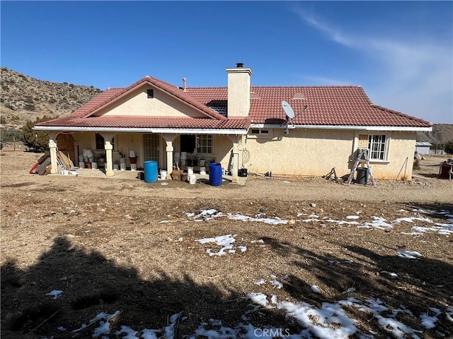 back of property featuring stucco siding, a chimney, and a tiled roof