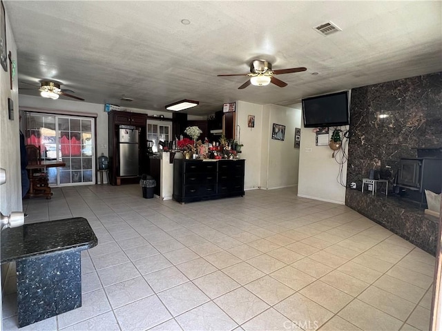 unfurnished living room featuring light tile patterned floors, visible vents, a wood stove, and a ceiling fan