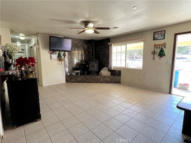 unfurnished living room featuring light tile patterned floors, a ceiling fan, a healthy amount of sunlight, and a wood stove