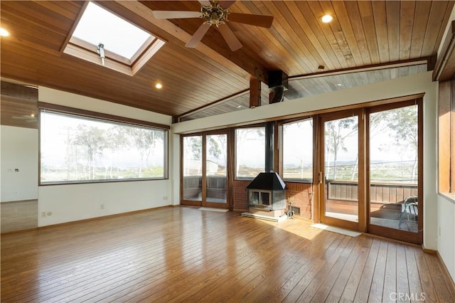 unfurnished sunroom with vaulted ceiling with skylight, wooden ceiling, a wood stove, and ceiling fan