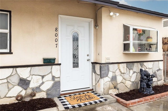 view of exterior entry with stucco siding and stone siding