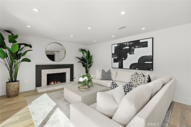 living area with recessed lighting, visible vents, wood finished floors, and a high end fireplace