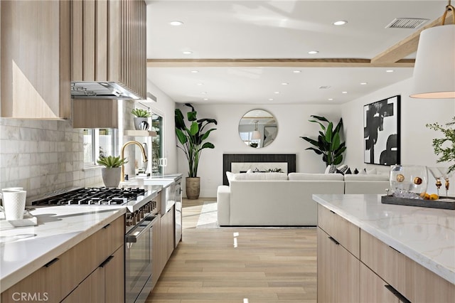 kitchen with high end stainless steel range oven, light brown cabinets, light wood-type flooring, modern cabinets, and backsplash