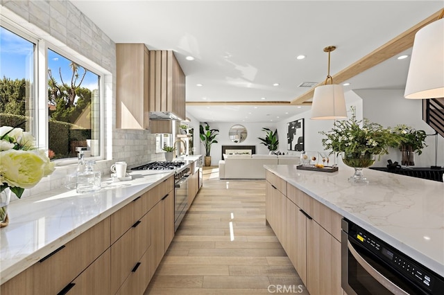 kitchen featuring high end stove, modern cabinets, light brown cabinets, light stone counters, and decorative backsplash