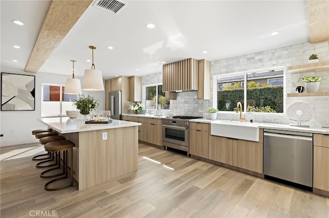 kitchen featuring visible vents, light wood finished floors, a sink, decorative backsplash, and high quality appliances