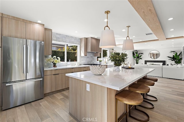 kitchen featuring visible vents, a kitchen island, light brown cabinetry, freestanding refrigerator, and modern cabinets