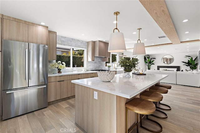 kitchen featuring decorative backsplash, a kitchen island, freestanding refrigerator, light brown cabinetry, and modern cabinets