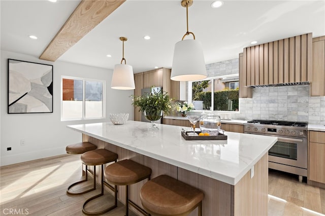 kitchen featuring light stone counters, gas stove, light wood finished floors, backsplash, and a center island