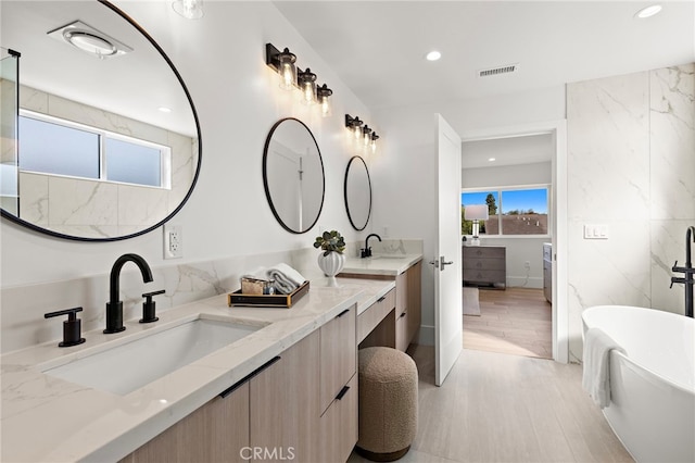 bathroom featuring a sink, double vanity, visible vents, a soaking tub, and wood finished floors