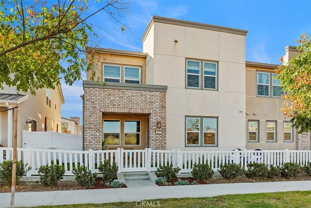 view of front of home with brick siding, a fenced front yard, and stucco siding