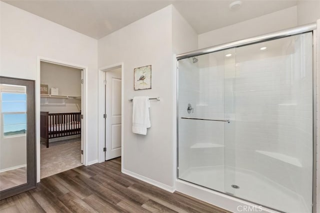 bathroom with a spacious closet, a stall shower, baseboards, and wood finished floors