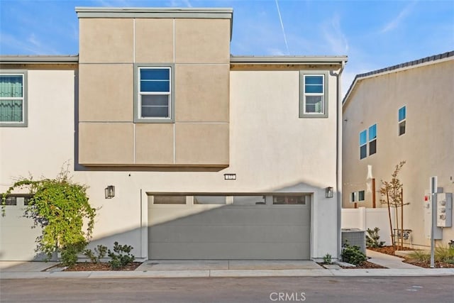 view of property with central air condition unit, an attached garage, fence, and stucco siding