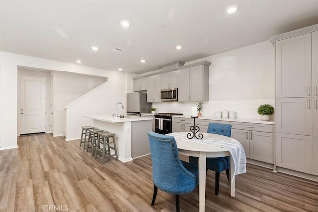 kitchen featuring black stove, a kitchen island with sink, a sink, stainless steel microwave, and freestanding refrigerator