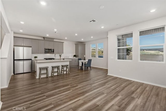 kitchen with visible vents, an island with sink, gray cabinets, dark wood-style flooring, and stainless steel appliances