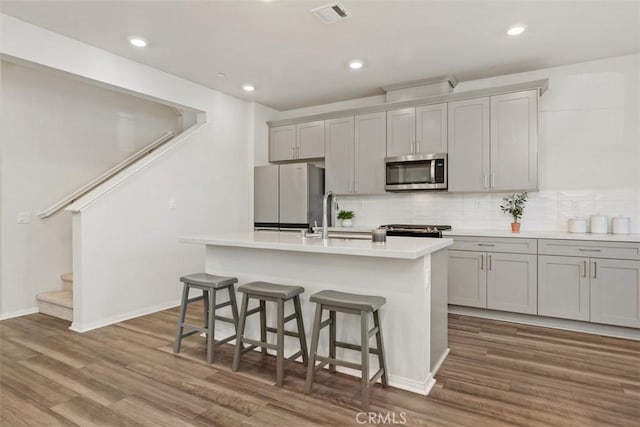 kitchen with visible vents, a kitchen bar, a kitchen island with sink, a sink, and appliances with stainless steel finishes