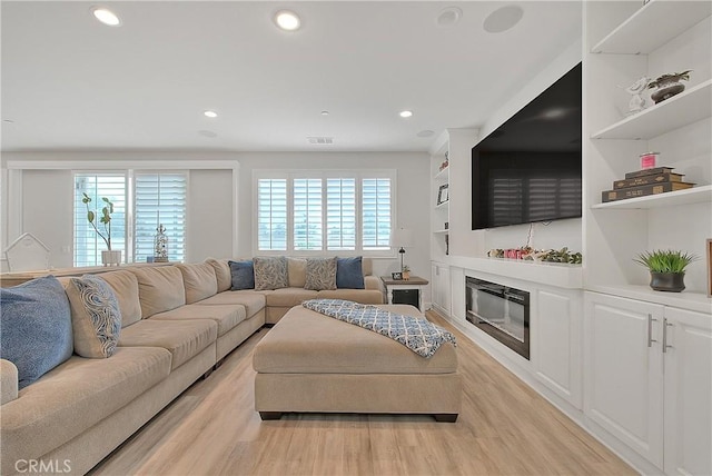 living area featuring a glass covered fireplace, recessed lighting, visible vents, and light wood finished floors