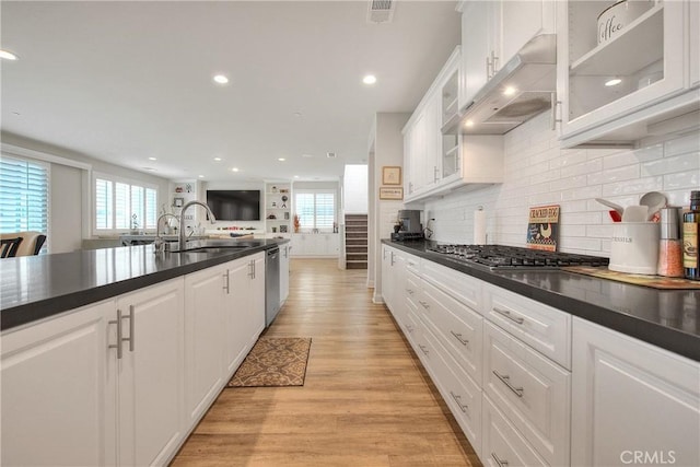 kitchen with under cabinet range hood, light wood finished floors, dark countertops, and a sink