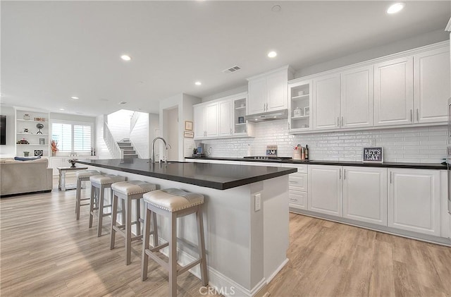 kitchen with visible vents, under cabinet range hood, dark countertops, light wood-style floors, and a breakfast bar area