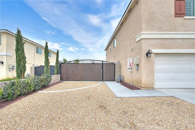 view of side of property with stucco siding, an attached garage, and a gate