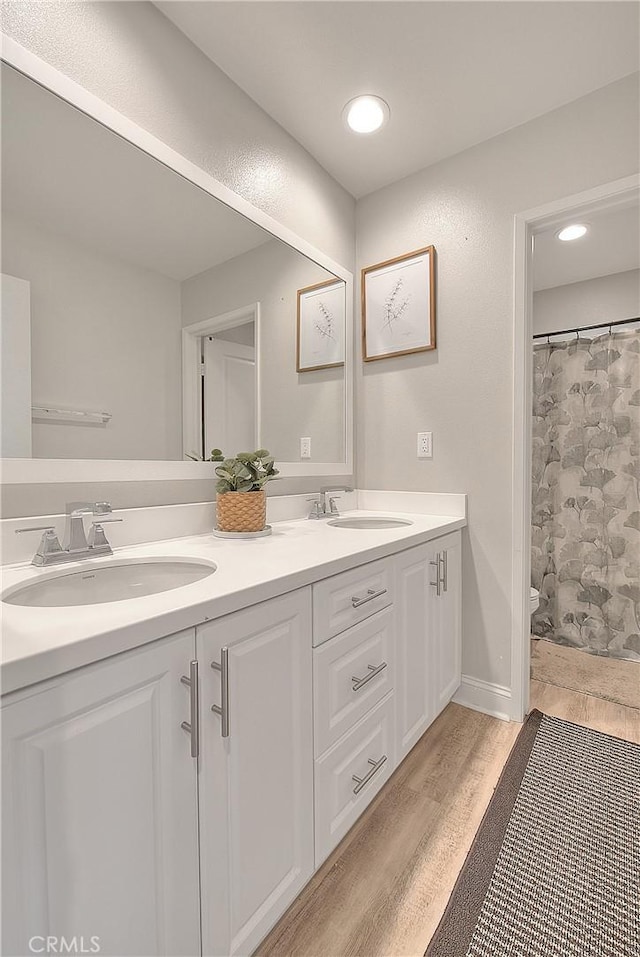 full bath with a sink, toilet, wood finished floors, and double vanity